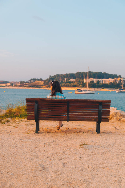 junge Frau, die auf der Bank sitzt und den Sonnenuntergang in der Meeresbucht betrachtet. Yachten im Hintergrund - Foto, Bild