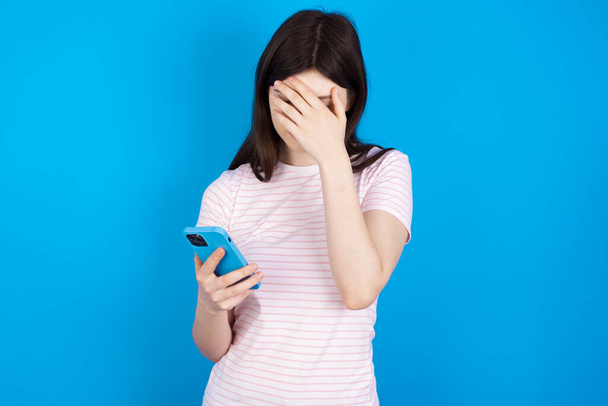 mladá brunetka žena při pohledu na chytrý telefon pocit smutné držení za ruku na tváři. - Fotografie, Obrázek