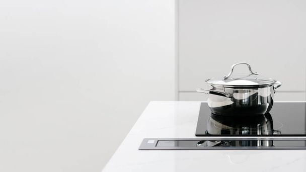 Metal pot being heated on fancy glass induction stove that is built in white counter, cooking food on reliable ceramic electric cooktop, kitchen with simple modern design - 写真・画像