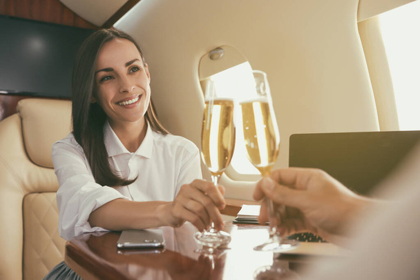 Colleagues clinking glasses of champagne at table in airplane during flight - Foto, Bild