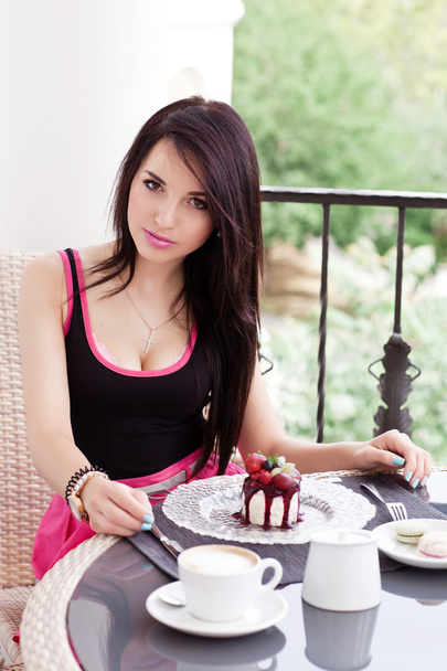Young beautiful woman eating a dessert and drink cappuccino at cafe with nice view - Photo, Image