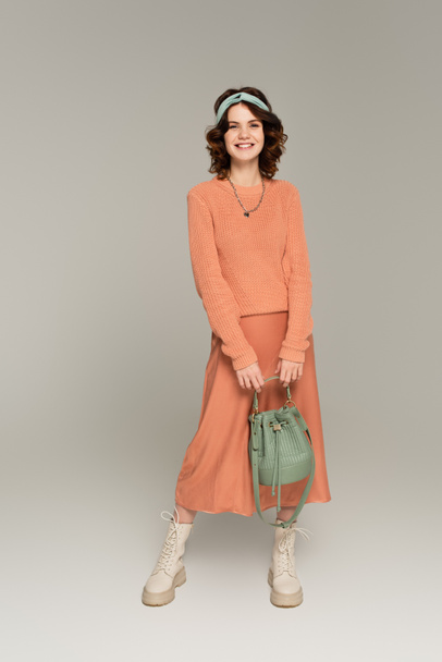 full length of happy woman in headband holding bag while standing on grey  - Foto, Imagem