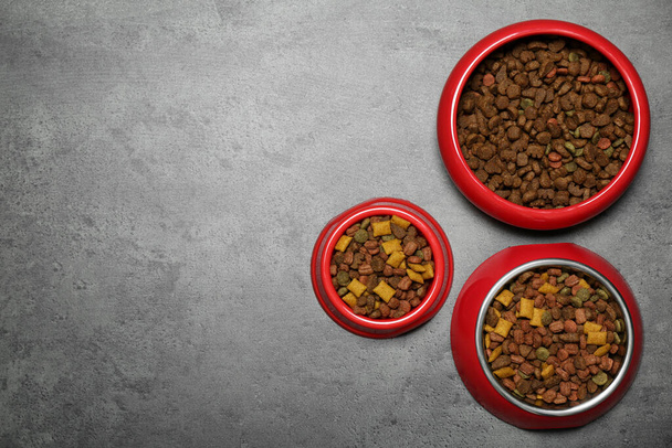 Pet bowls with dry food on grey background, flat lay. Space for text - Photo, Image