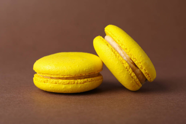 Delicious yellow macarons on brown background, closeup - 写真・画像