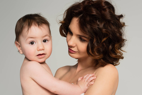 caring mother with bare shoulders looking at toddler son isolated on grey - Foto, Bild
