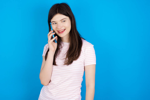 Pleasant looking happy young brunette woman has nice telephone conversation and looks aside, has nice mood and smiles positively while talks via cell phone - Fotoğraf, Görsel