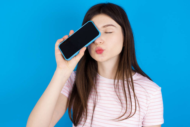 Adorable young brunette woman holding modern device covering eye with lips pouted - Photo, Image