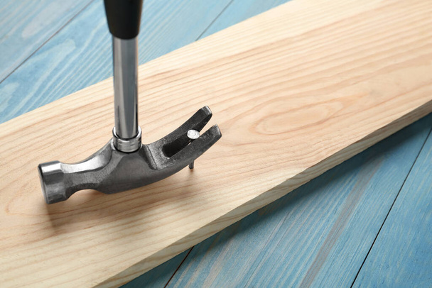 Hammer pulling metal nail out of plank on light blue table, closeup - Foto, Imagem