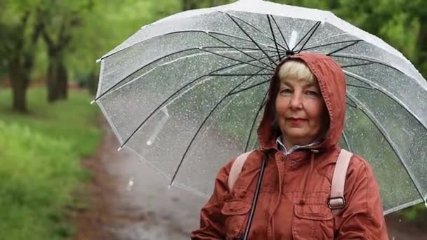 Açık havada yağmur altında şeffaf şemsiyeli mutlu bir kadın. - Video, Çekim