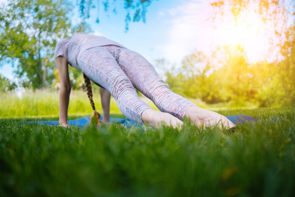 Nuori nainen harrastaa joogaa puistossa. tyttö venyttely liikunta jooga asennossa. onnellinen ja terve nainen istuu lootuksen asennossa ja harjoittelee joogaa. meditaatio ja urheilu auringonlaskussa ulkona. - Valokuva, kuva