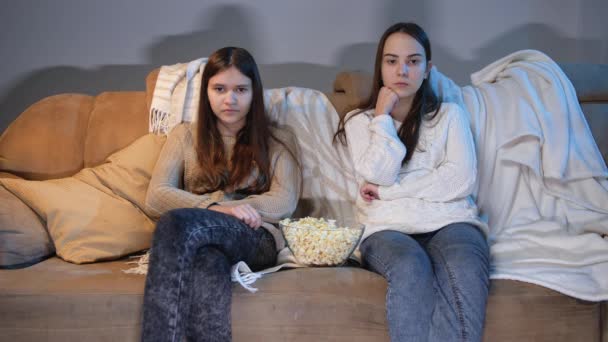 İki genç kız kanepede televizyon izliyor ve geceleri patlamış mısır yiyor. - Video, Çekim