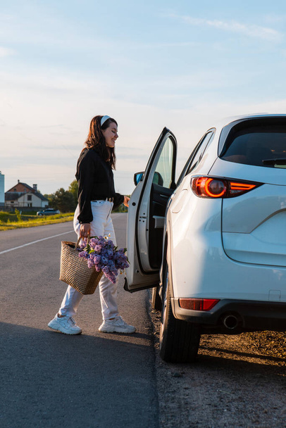 woman with basket of flowers sitting in car parked at road side - Photo, Image