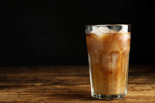 Glass of coffee with milk and ice cubes on wooden table. Space for text - Fotó, kép