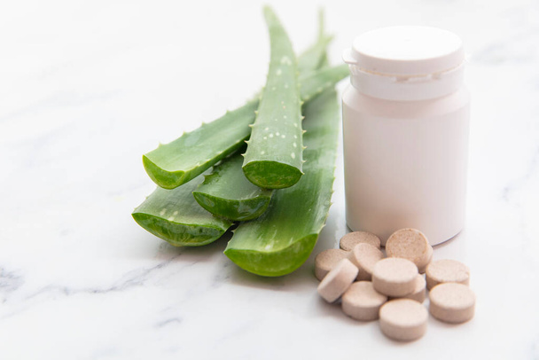 Aloe vera natural tablets. Freshly cut leaves with a pill bottle and tablets - Foto, Imagen