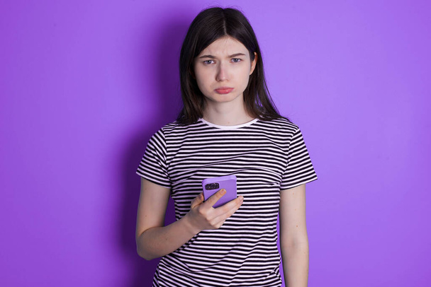 Ontevreden jonge brunette vrouw maakt gebruik van mobiele software applicatie en surft informatie op internet, houdt moderne mobiele hand - Foto, afbeelding