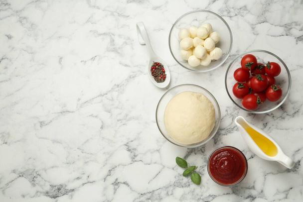 Raw pizza dough and other ingredients on white marble table, flat lay. Space for text - Valokuva, kuva