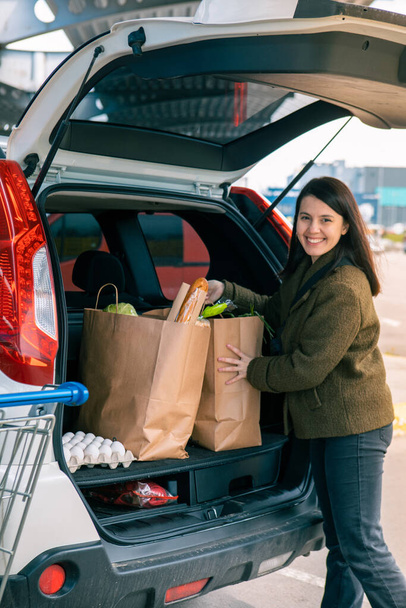 hymyilevä nainen laittaa laukkuja tuotteita auton takakonttiin jälkeen ruokakauppa kopioi tilaa - Valokuva, kuva