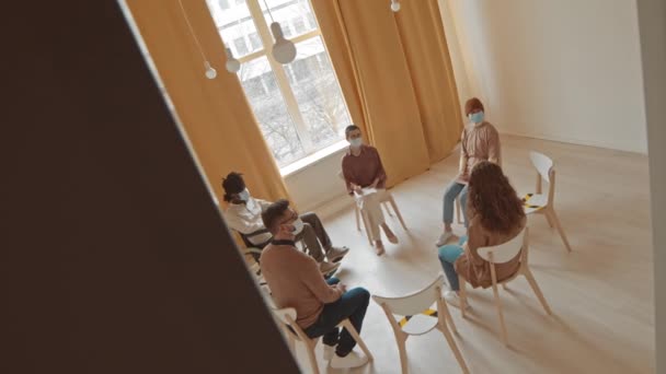 Imagem de rastreamento de alto ângulo de diversas pessoas com problemas mentais ou de saúde tendo sessão de terapia de grupo com psicologia feminina sentados juntos em círculo em sala brilhante - Filmagem, Vídeo