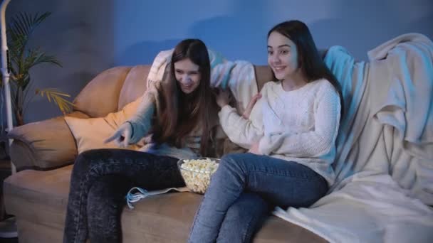 Dos chicas riendo divirtiéndose mientras ven comedia o video divertido en la televisión por la noche - Metraje, vídeo