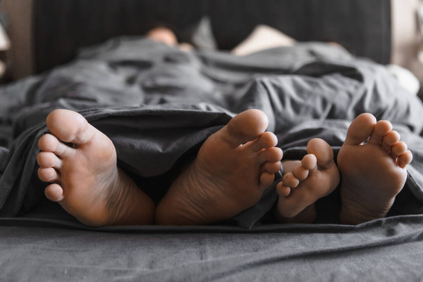 par de pies debajo de la manta en la cama con sábanas grises cerrar espacio de copia - Foto, Imagen