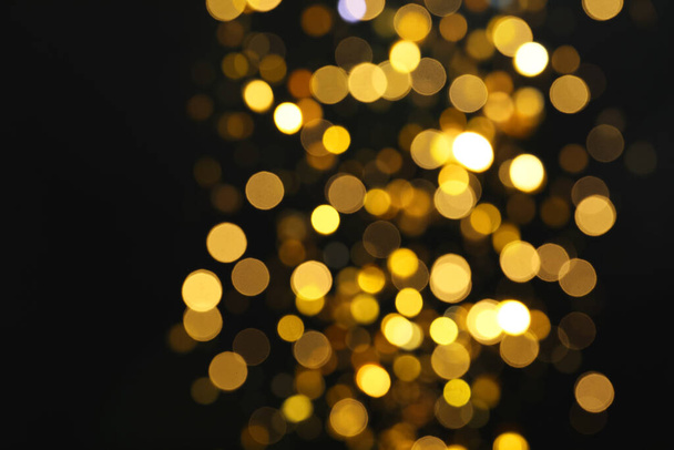 Blurred view of golden lights on black background. Bokeh effect - Фото, зображення