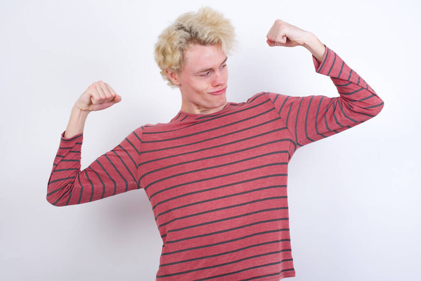 jeune homme blond montrant les muscles des bras souriant fier. Concept de fitness. - Photo, image
