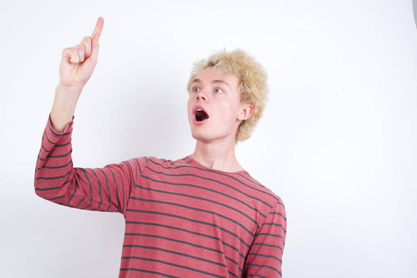 young blond man pointing finger up and looking inspired by genius thought, showing good idea sign, having clever solution in mind - Photo, Image