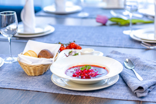 Cékla leves, borscsé, gyönyörűen tálalva egy fehér tányérral az asztalon.  - Fotó, kép