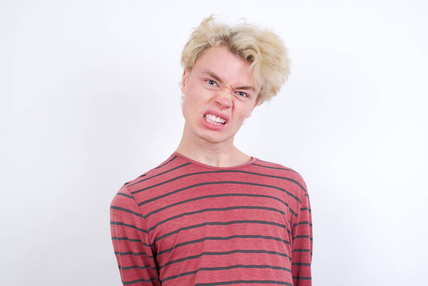 jonge blonde man houdt tanden gebald, fronst gezicht in ontevredenheid, geïrriteerd vanwege veel plichten. - Foto, afbeelding