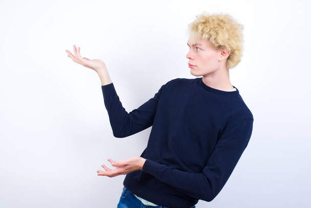 Mladý blonďatý muž ukazuje oběma rukama na něco divného a říká: Nevím, co to je. Koncept reklamy. - Fotografie, Obrázek