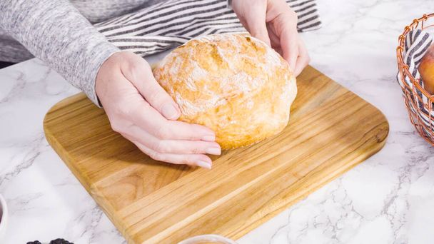 Step by step. Slicing a loaf of ciabatta bread with a bread knife on a wood cutting board. - Photo, Image