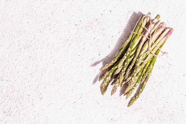 Ripe asparagus on a white textured plaster background. Fresh green ingredients ready for cooking healthy food. A modern hard light, dark shadow, top view - Foto, immagini