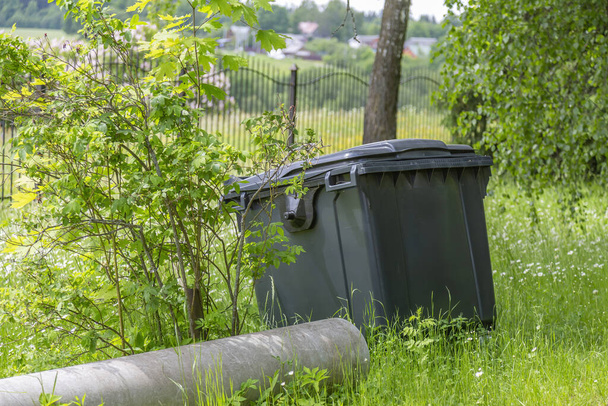 A large plastic garbage container stands in a green summer forest - Foto, imagen