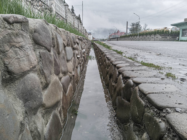 Decorative drain ditch with walls lined with stone boulders near the road, close-up. - Zdjęcie, obraz