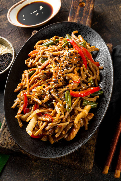 Plate of asian buckwheat soba noodles with vegetables, mushrooms and chicken on dark background close up vertical photo - Zdjęcie, obraz