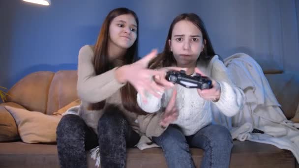 Δύο συμπυκνωμένα κορίτσια που παίζουν βιντεοπαιχνίδια στην κονσόλα παιχνιδιών στο σαλόνι τη νύχτα - Πλάνα, βίντεο