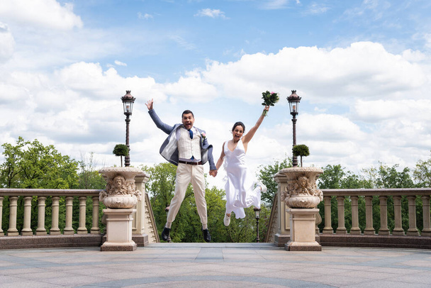 Happy newlyweds with bouquet jumping in park  - Valokuva, kuva