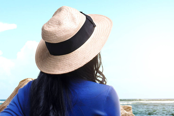 Rear view of an Asian woman with hat looking at view on the beach with blue sky background - Foto, Imagem