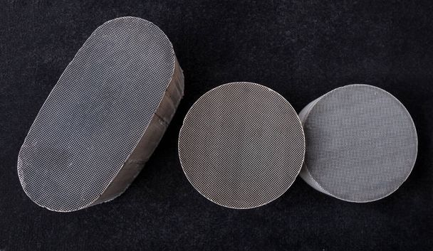 drei runde und ovale Keramikkatalysatoren mit Platin, Palladium und Rhodium auf schwarzem Hintergrund. Verarbeitung und Annahme von Nichteisenmetallen. - Foto, Bild