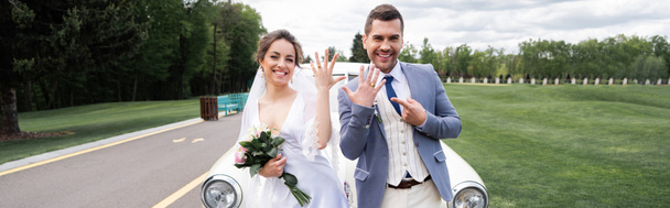 Cheerful groom pointing at ring near bride with bouquet and vintage car, banner  - Foto, Imagen