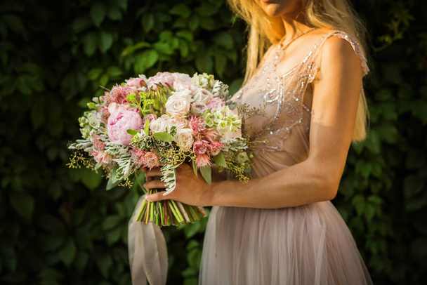 Portrait of an elegant unrecognizable pretty woman wearing grey wedding dress and posing in the street. Bride holds a bouquet of pastel flowers and greenery - Foto, Imagem
