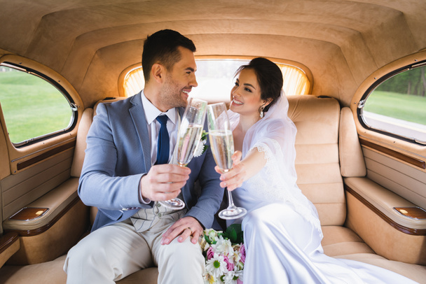 Gülümseyen yeni evliler arabalarında şampanya içerken birbirlerine bakıyorlar.  - Fotoğraf, Görsel