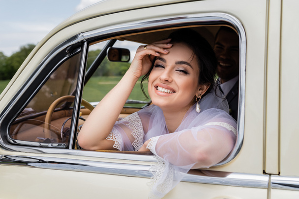 Щаслива наречена дивиться на камеру біля вікна старовинного авто
  - Фото, зображення