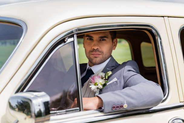 Elegant groom looking at camera in vintage car  - Fotó, kép