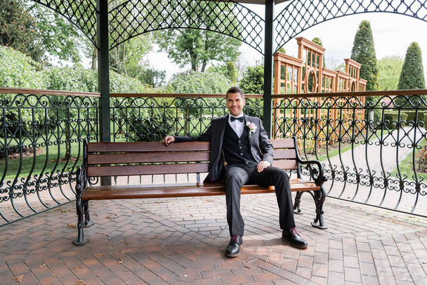 Smiling groom sitting on bench in park  - Fotoğraf, Görsel