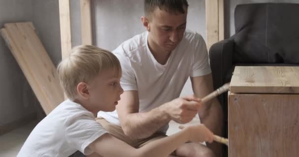 Young father carpenter teaching his son how to work with wood. Boy helps his dad in workshop. - Footage, Video