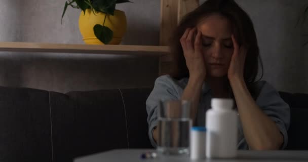Mladá žena trpící bolestí hlavy se dotkne spánků. Prášek vpředu na stole. - Záběry, video