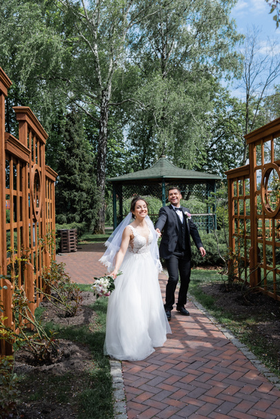 Gelukkige bruid en bruidegom wandelen op loopbrug in park  - Foto, afbeelding