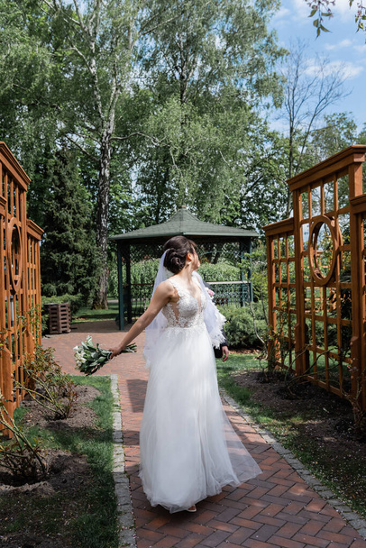 Junge Braut mit Blumenstrauß läuft in der Nähe des Bräutigams im Park  - Foto, Bild
