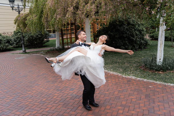 Щасливий наречений обертається наречена в білій весільній сукні в парку
  - Фото, зображення